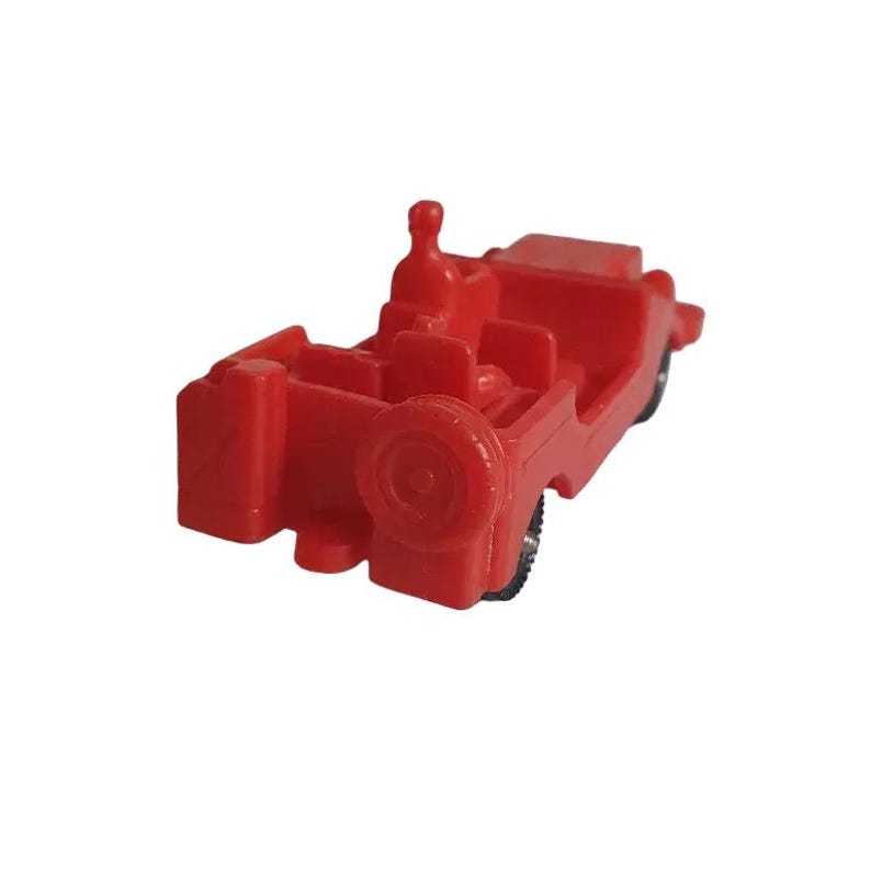 May include: A small, red toy car with a spare tire on the back. The miniature vehicle has a driver's seat and passenger seating. The wheels are black. The toy car is made of plastic.