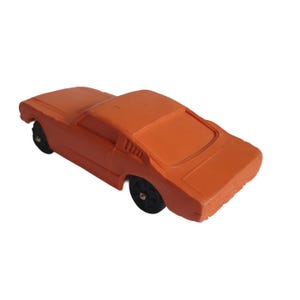 Puede incluir: Un coche de juguete naranja con ruedas negras. El coche cl&aacute;sico tiene una carrocer&iacute;a coup&eacute;. El coche de juguete es de color liso y parece estar hecho de pl&aacute;stico. El coche se ve desde un &aacute;ngulo alto.