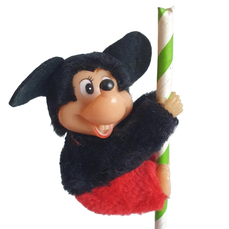 May include: A vintage Mickey Mouse toy figure, dressed in black and red, clinging to a green and white striped pole. The toy has a plastic face with a smiling expression and large black ears.