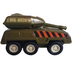 Puede incluir: Un tanque militar de juguete verde con rayas negras y naranjas, cuatro ruedas y una torreta giratoria con el texto "HQ 4929" en la parte superior.