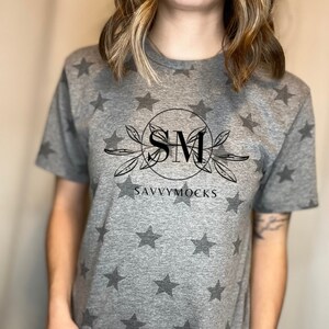 May include: Gray t-shirt with a black star pattern and a black graphic of a circle with the letters "SM" inside and the text "SAVVYMOCKS" below.