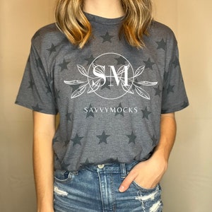 May include: A gray t-shirt with a white star pattern and a white circle with the letters "SM" inside. The text "SAVVYMOCKS" is below the circle.