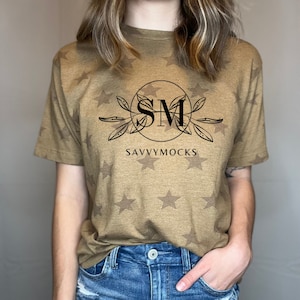 May include: A brown t-shirt with a white star pattern. The shirt has a black circle with the letters "SM" inside and the text "SAVVYMOCKS" below the circle.