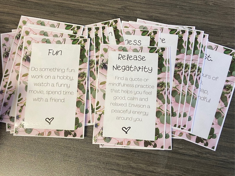 May include: A stack of pink and green cards with inspirational messages. The top card says "Release Negativity" and has a quote about mindfulness. The card below says "Fun" and has a list of activities to do for fun.