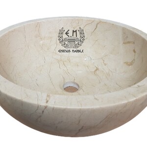 Pu&ograve; includere: Un lavabo rotondo in marmo bianco avorio con un foro di scarico al centro. Il lavabo ha una superficie liscia e lucida con venature sottili. Il lavabo &egrave; realizzato da Ephesus Marble.
