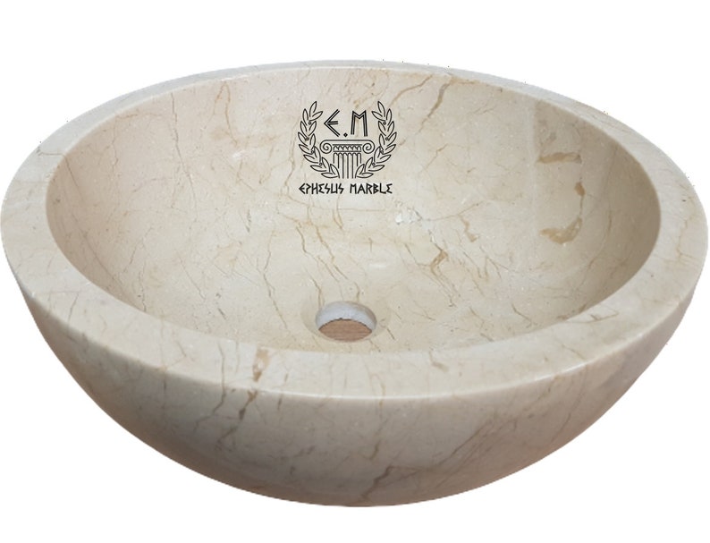 Pu&ograve; includere: Un lavabo rotondo in marmo bianco avorio con un foro di scarico al centro. Il lavabo ha una superficie liscia e lucida con venature sottili. Il lavabo &egrave; realizzato da Ephesus Marble.