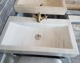 Pode incluir: Pia de banheiro de mármore branco com uma torneira dourada e uma tampa de drenagem cromada.