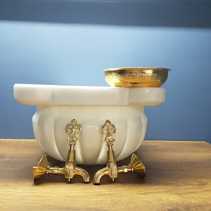 Op de afbeelding: Wit marmeren voetbad met twee gouden kranen en een gouden kom bovenop.