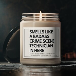 May include: A beige candle with a white label that reads "Smells like a badass crime scene technician in here. Light this candle when you are feeling especially badass."