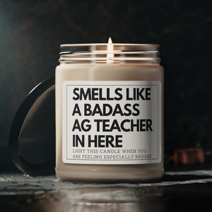 May include: A beige candle with a black label that reads "Smells like a badass AG teacher in here. Light this candle when you are feeling especially badass."