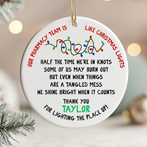 May include: A round white ceramic ornament hanging by a gold string. It features a colorful string of Christmas lights graphic and black text that reads: Our pharmacy team is like Christmas lights, half the time we're in knots, some of us may burn out, but even when things are a tangled mess, we shine bright when it counts, thank you Taylor for lighting the place up!
