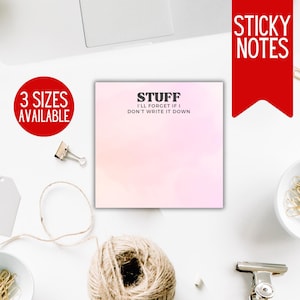 May include: A set of pink sticky notes with the text "STUFF I'LL FORGET IF I DON'T WRITE IT DOWN" in black. The sticky notes are on a white surface with various office supplies, including gold paper clips, twine, and a laptop.