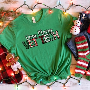 May include: A green t-shirt with the text "Very Merry VET TECH" in a festive design. The image includes a pair of blue jeans, red and green striped socks, a small gift box, and Christmas decorations.