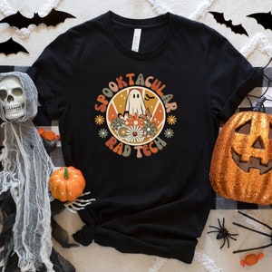 Puede incluir: Camiseta negra con un gráfico retro de un fantasma con el texto "Spooktacular Rad Tech" en un círculo.