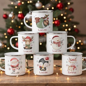 May include: White enamel mugs with Christmas-themed illustrations of a sloth, reindeer, snowman, Santa, penguin, and deer. Each mug has a name printed on it, such as "Lucas" or "Jacob". The mugs are arranged on a wooden surface with a Christmas tree in the background.