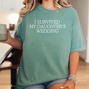 May include: A teal blue t-shirt with the text "I survived my daughter's wedding" in white.