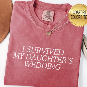 May include: A red t-shirt with the text "I survived my daughter's wedding" in white lettering. The shirt is made by Comfort Colors.