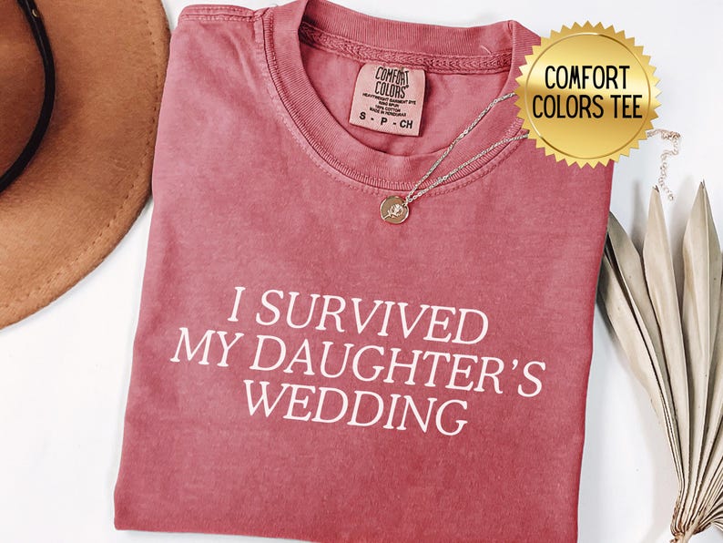 May include: A red t-shirt with the text "I survived my daughter's wedding" in white lettering. The shirt is made by Comfort Colors.