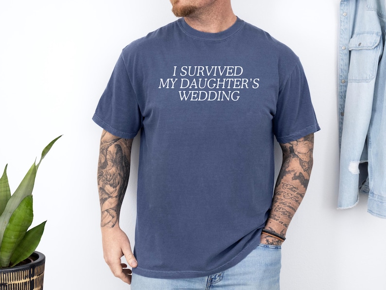 May include: A navy blue t-shirt with the text "I survived my daughter's wedding" printed in white.