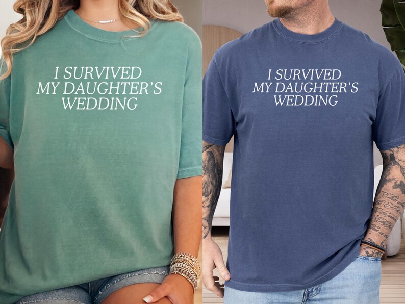 May include: Two t-shirts with the text "I survived my daughter's wedding" in white lettering. The shirt on the left is teal green and the shirt on the right is navy blue.