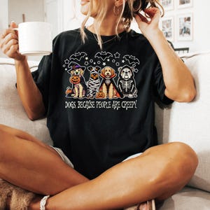 May include: Black t-shirt featuring a Halloween-themed graphic of four dogs dressed in costumes, including a witch, mummy, vampire, and skeleton. The text "DOGS BECAUSE PEOPLE ARE CREEPY" is below the dogs.