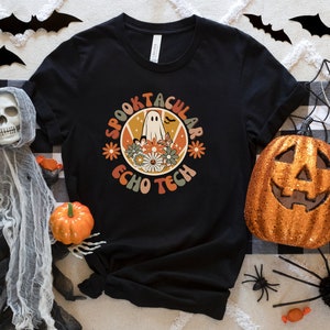 Peut inclure: T-shirt noir avec un graphique rétro d'un fantôme avec le texte "Spooktacular Echo Tech" en orange et jaune.