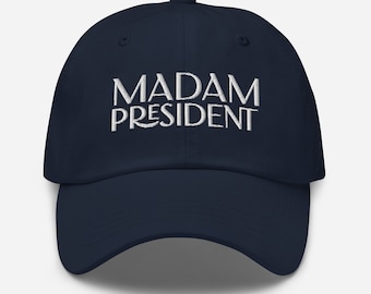 以下が含まれることがあります： 「MADAM PRESIDENT」と白く刺繍された文字が入った紺色のベースボールキャップです。