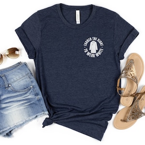 May include: A navy blue t-shirt with a white circle graphic that says "Earned the Right to Wear White" with a white outline of a doctor's coat inside the circle. The t-shirt is paired with denim shorts and gold sandals.