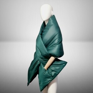 May include: A dark green quilted scarf or shawl is draped around a mannequin. The scarf is made of a soft, puffy material and has a unique, asymmetrical design.