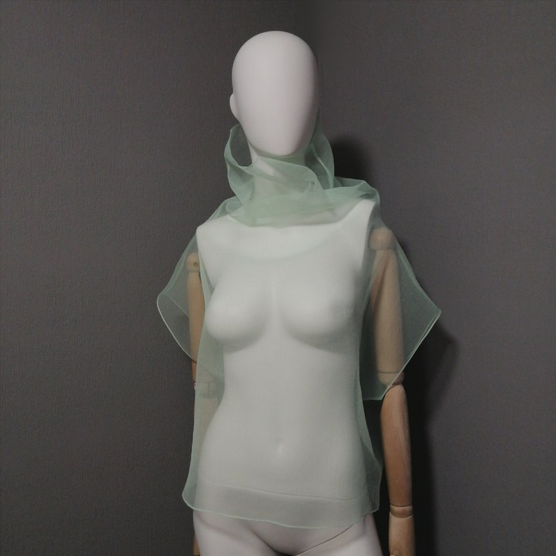 Puede incluir: Una blusa transparente de color verde claro con cuello alto y mangas cortas. La blusa est&aacute; hecha de una tela delicada y fluida, perfecta para superponer.