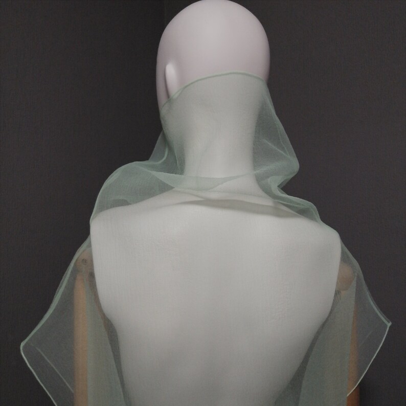 Puede incluir: Una estola de gasa verde claro drapeada sobre los hombros de un maniqu&iacute;. La estola est&aacute; hecha de una tela delicada y ligera y tiene un drapeado fluido y elegante.