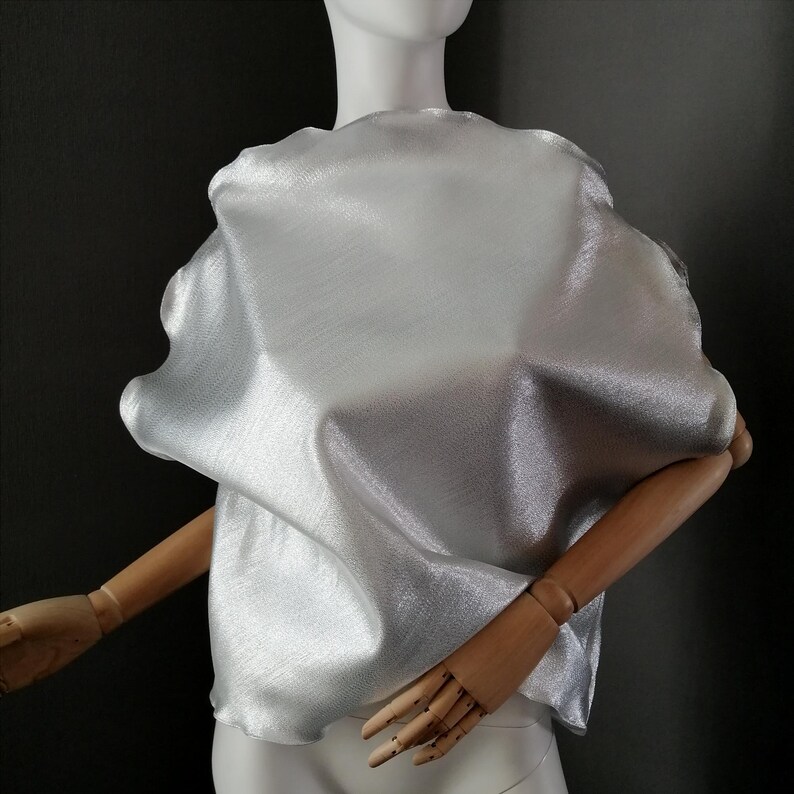 May include: A silver metallic fabric top with a loose, flowing fit. The fabric has a subtle sheen and a slightly wrinkled texture.