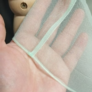 Puede incluir: Primer plano de una tela transparente verde claro con un ribete blanco. La tela est&aacute; doblada sobre s&iacute; misma, mostrando las costuras a lo largo del borde.