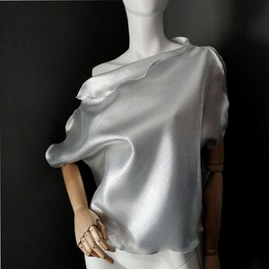 May include: A silver metallic off-the-shoulder top with a draped design.