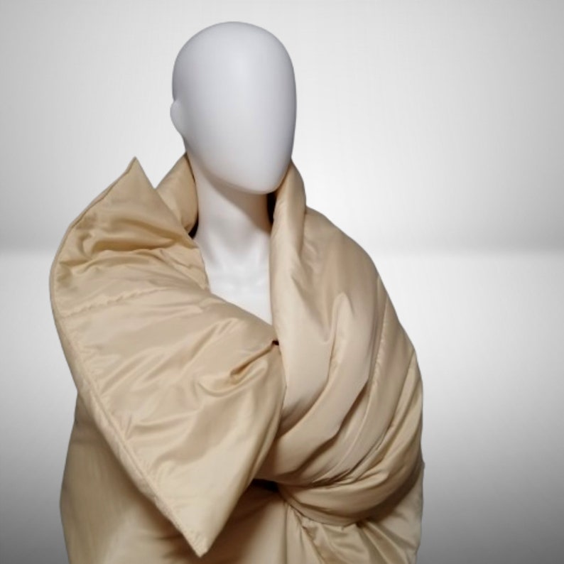 May include: A beige quilted blanket draped over a mannequin. The blanket is made of a soft, luxurious fabric and has a simple, elegant design.