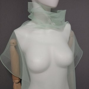 Puede incluir: Una estola de gasa verde claro drapeada sobre un maniqu&iacute; blanco. La estola est&aacute; hecha de una tela delicada y fluida.