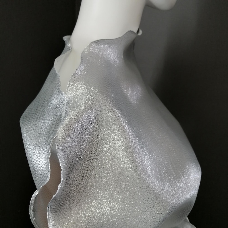 May include: A silver metallic fabric with a textured surface. The fabric has a scalloped edge and is draped over a form.