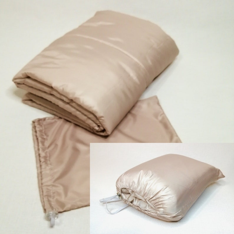 May include: A beige quilted blanket folded in half and placed on a white surface. The blanket is shown in two different configurations: folded and rolled up. The blanket is made of a soft, lightweight material and is perfect for keeping warm on chilly nights.