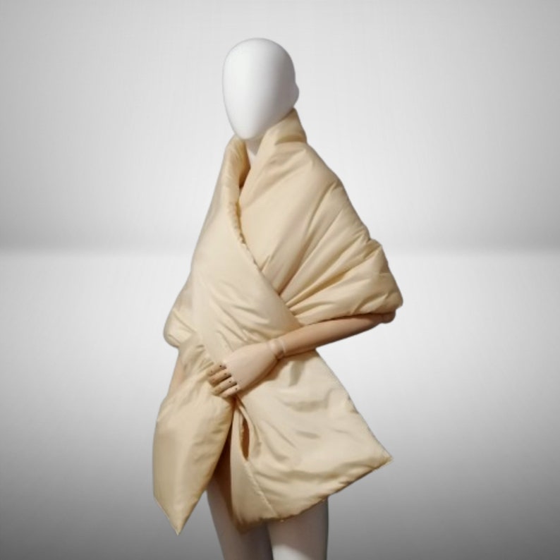 May include: A cream-colored quilted shawl draped over a mannequin. The shawl is made of a soft, luxurious fabric and has a simple, elegant design.