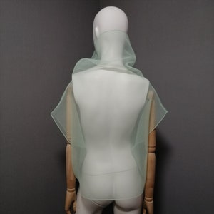 Puede incluir: Una bufanda de gasa verde claro drapeada sobre un maniqu&iacute; blanco. La bufanda est&aacute; hecha de una tela ligera y transl&uacute;cida y tiene un dise&ntilde;o fluido y drapeado.