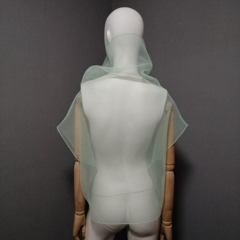 Puede incluir: Una bufanda de gasa verde claro drapeada sobre un maniqu&iacute; blanco. La bufanda est&aacute; hecha de una tela ligera y transl&uacute;cida y tiene un dise&ntilde;o fluido y drapeado.