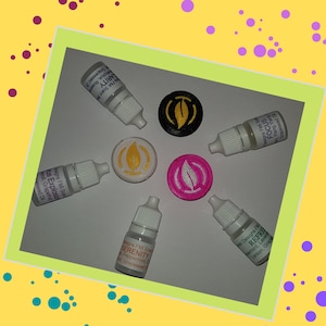 Op de afbeelding: Vijf kleine flesjes met essentiële oliemengsels met etiketten waarop "Serenity", "Focus", "Clarity", "Refresh" en "Citrus Explosion" staat. Elk flesje bevindt zich naast een kleine ronde schijf met een bladerenontwerp in zwart, wit, roze en goud.