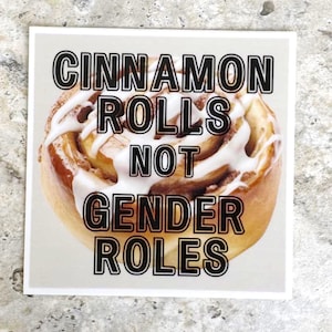 May include: Square sticker featuring a cinnamon roll with white icing. The text on the sticker reads "CINNAMON ROLLS NOT GENDER ROLES" in bold, black letters. The sticker is on a light gray background.