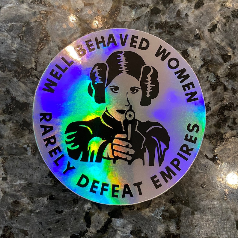 May include: A round, iridescent sticker with the text "Well Behaved Women Rarely Defeat Empires" and a black and white image of Princess Leia holding a blaster.