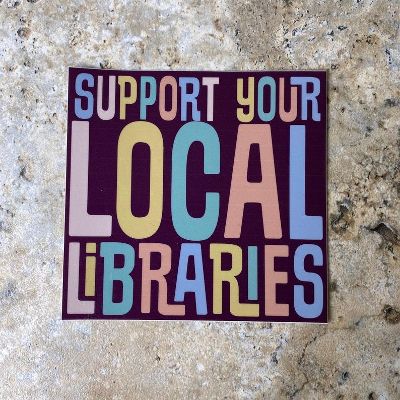 May include: A sticker with the text "Support Your Local Libraries" in colorful letters on a dark purple background.