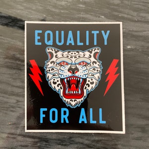 May include: Square sticker with a black background and the words "EQUALITY FOR ALL" in blue. A white and black spotted leopard head is centered above the words. Red lightning bolts are on either side of the leopard head.