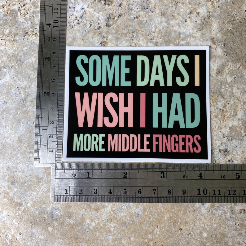 K&ouml;nnte beinhalten: Ein schwarzer Aufkleber mit wei&szlig;em Text, der "Some days I wish I had more middle fingers" lautet. Der Text ist in einem Regenbogen-Farbschema mit Gr&uuml;n, Rosa und Hellblau gehalten.