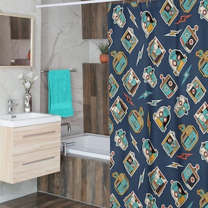 May include: A navy blue shower curtain with a repeating pattern of retro robots in teal, yellow, and white, along with lightning bolt graphics. The curtain is hanging in a bathroom with a light wood vanity and a teal towel.
