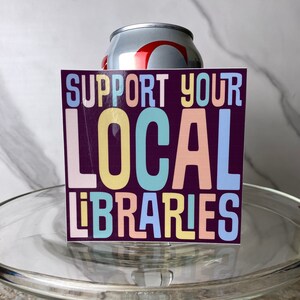 May include: A sticker with the text "Support Your Local Libraries" in colorful letters on a dark purple background.