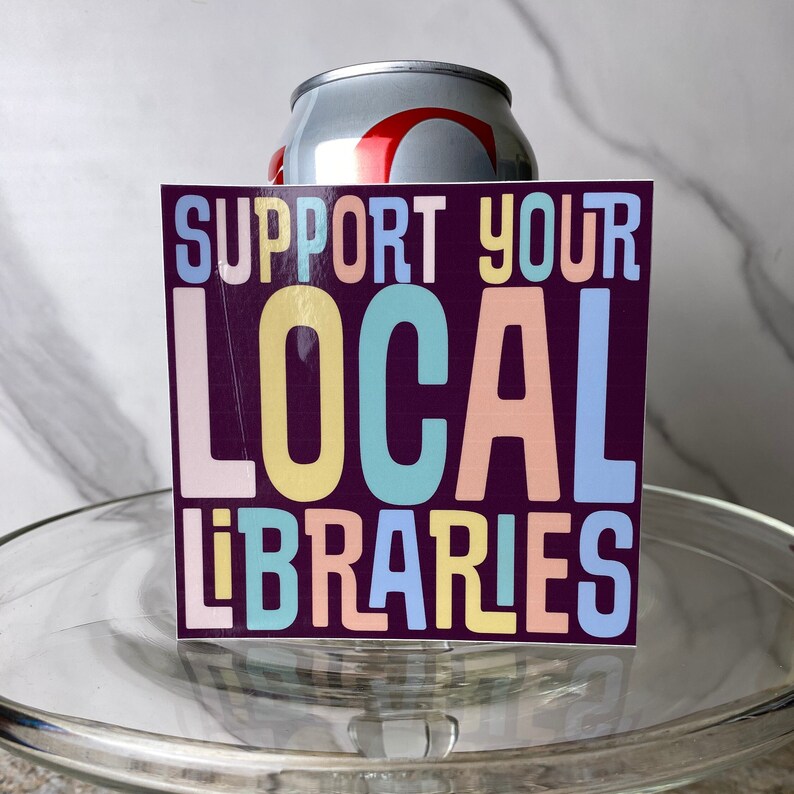 May include: A sticker with the text "Support Your Local Libraries" in colorful letters on a dark purple background.